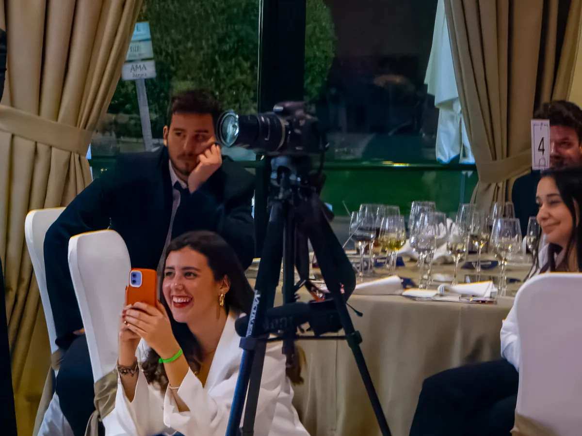 Una cámara sobre un trípode y una invitada grabando con el móvil